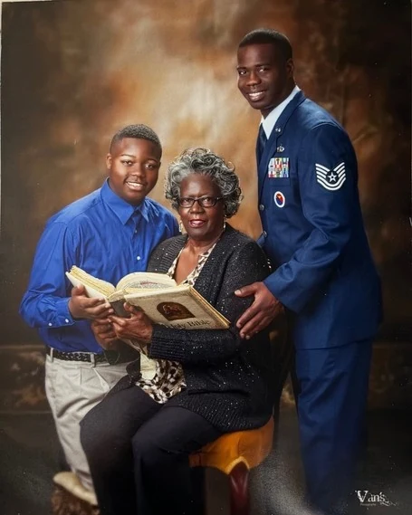 A studio portrait of Chief Seals in dress blues standing behind his family, seated with an album.