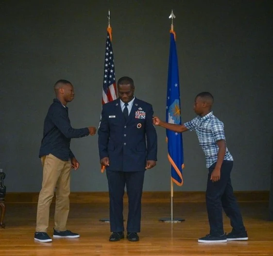 Chief Seals in service dress between the United States and Air Force flags with his sons.